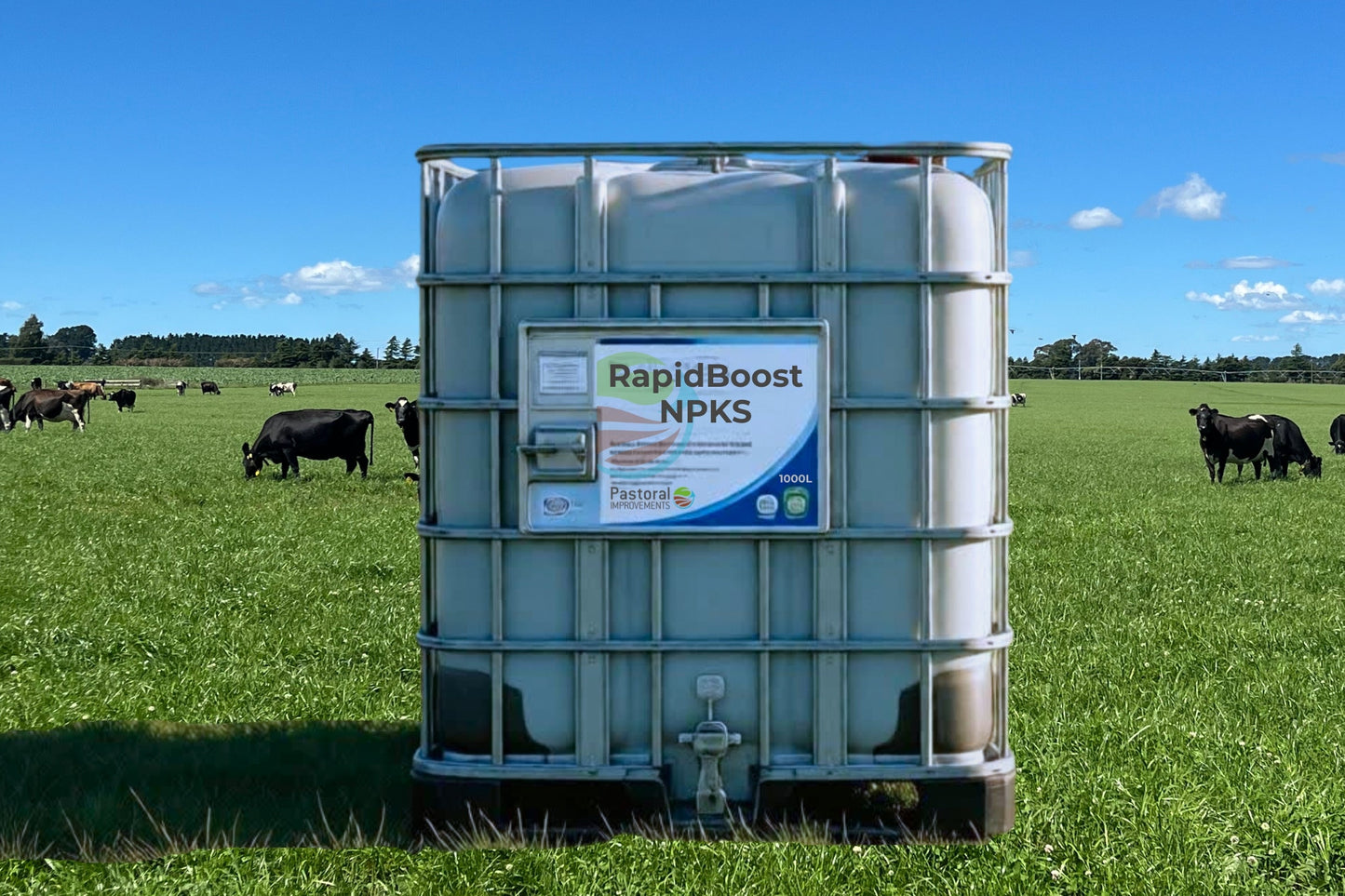 Large container labeled 'RapidBoost NPKS' in a field with cows under a blue sky.